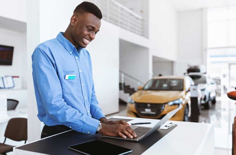 A buyer and seller reviewing a vehicle price worksheet beside a parked car.